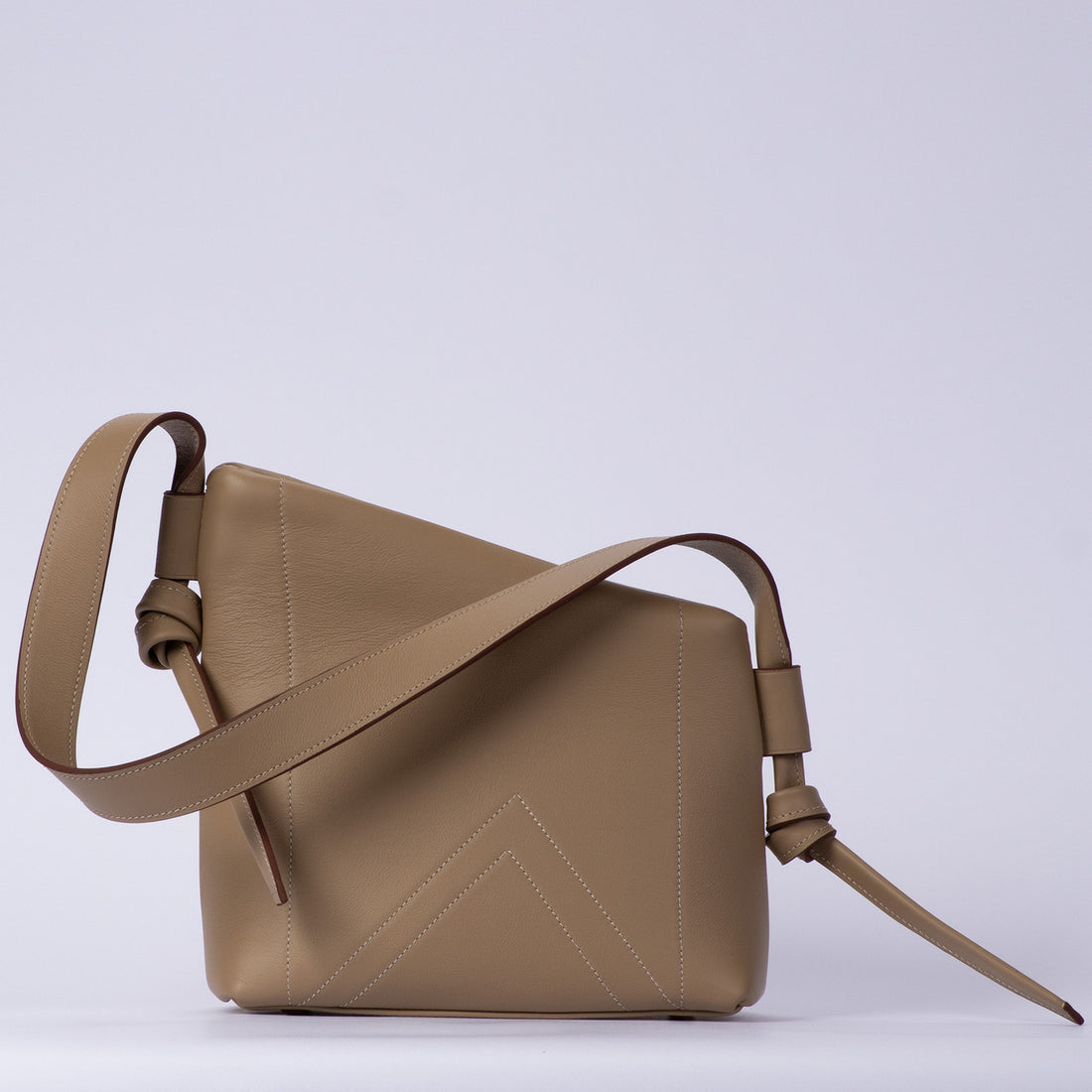 Muted Light Dove Beige Asymmetrical Sculptural Shoulder Bag With Double Chevron Front Stitching, Decorative Knotted Side Carry Straps And Slanted Soft Silhouette
