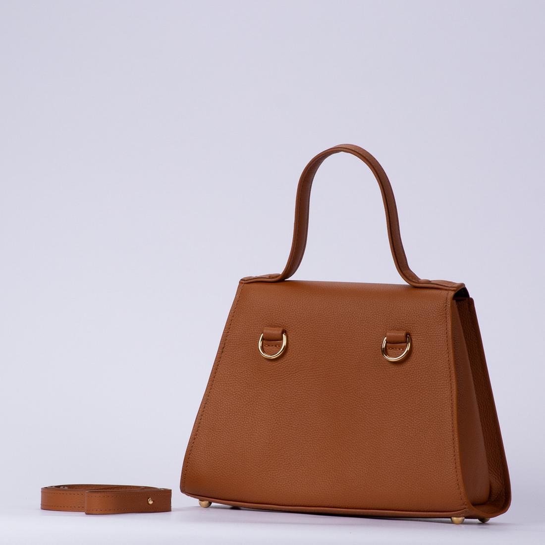 Warm Sienna Tan Textured Trapezoid Top Handle Handbag With Curved Flap Golden Ring Clasp, Base Protective Metal Studs And Side Mount Hardware Loops